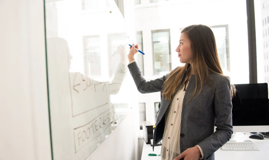 A woman wearing a blazer and writing on a whiteboard