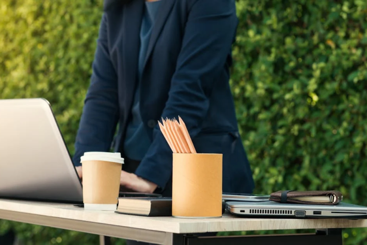 A gray laptop on a table, with a cup of pencils and a coffee cup