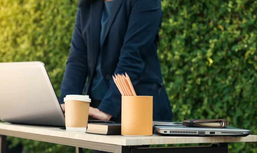 A gray laptop on a table, with a cup of pencils and a coffee cup