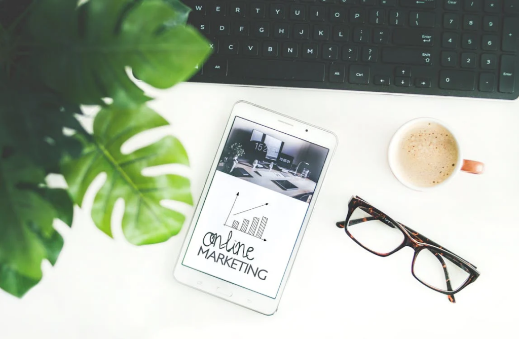 A tablet next to a plant, pair of glasses, and cup of coffee