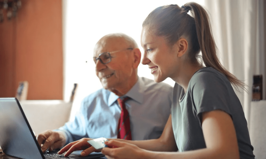 A woman sitting next to an elderly man while they look at a laptop