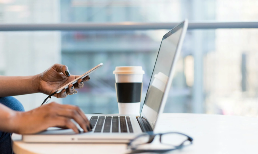 A woman working on a laptop and holding a smartphone