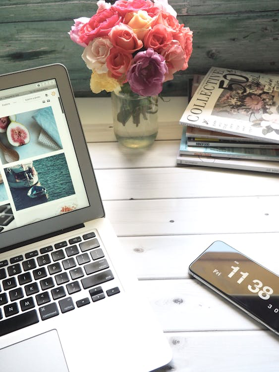 A laptop on a desk, next to a smartphone with the time